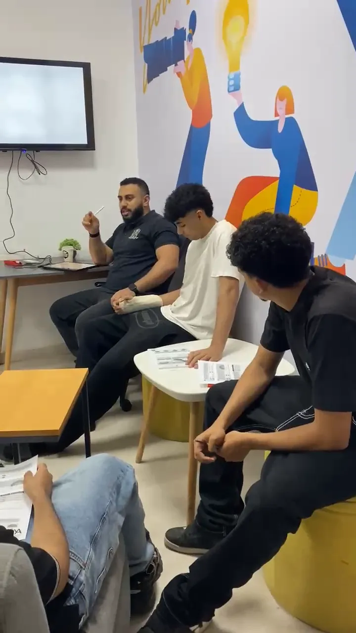 Yousef sitting with a pen raised mid-sentence while three students listen.