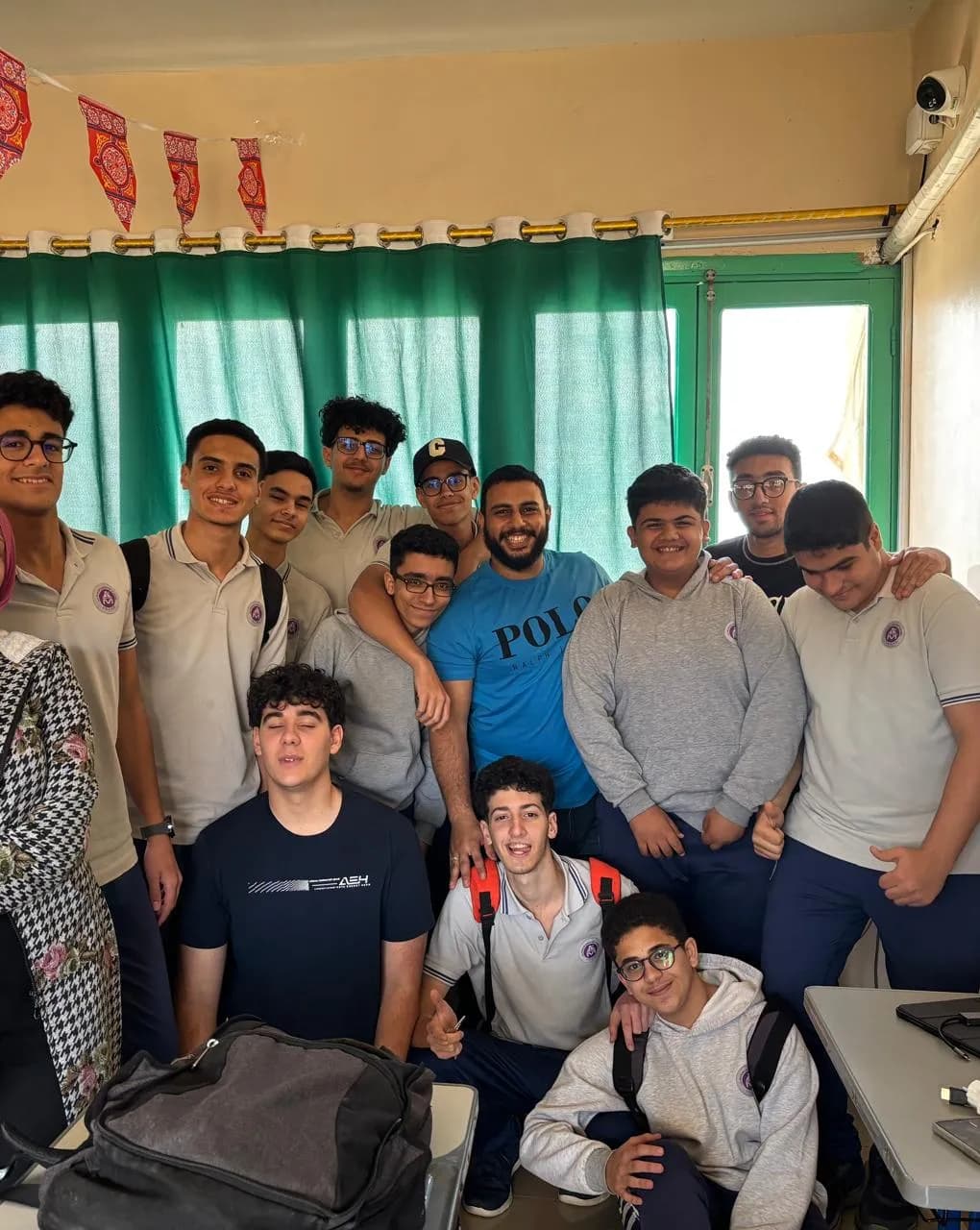 Yousef Mohamed standing among a full group of his students in their classroom, most of them in school uniform.