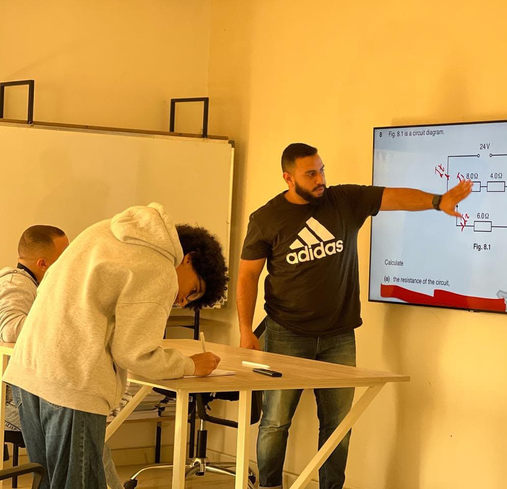 Yousef pointing to a circuit diagram on screen while a student works through the question at the table.