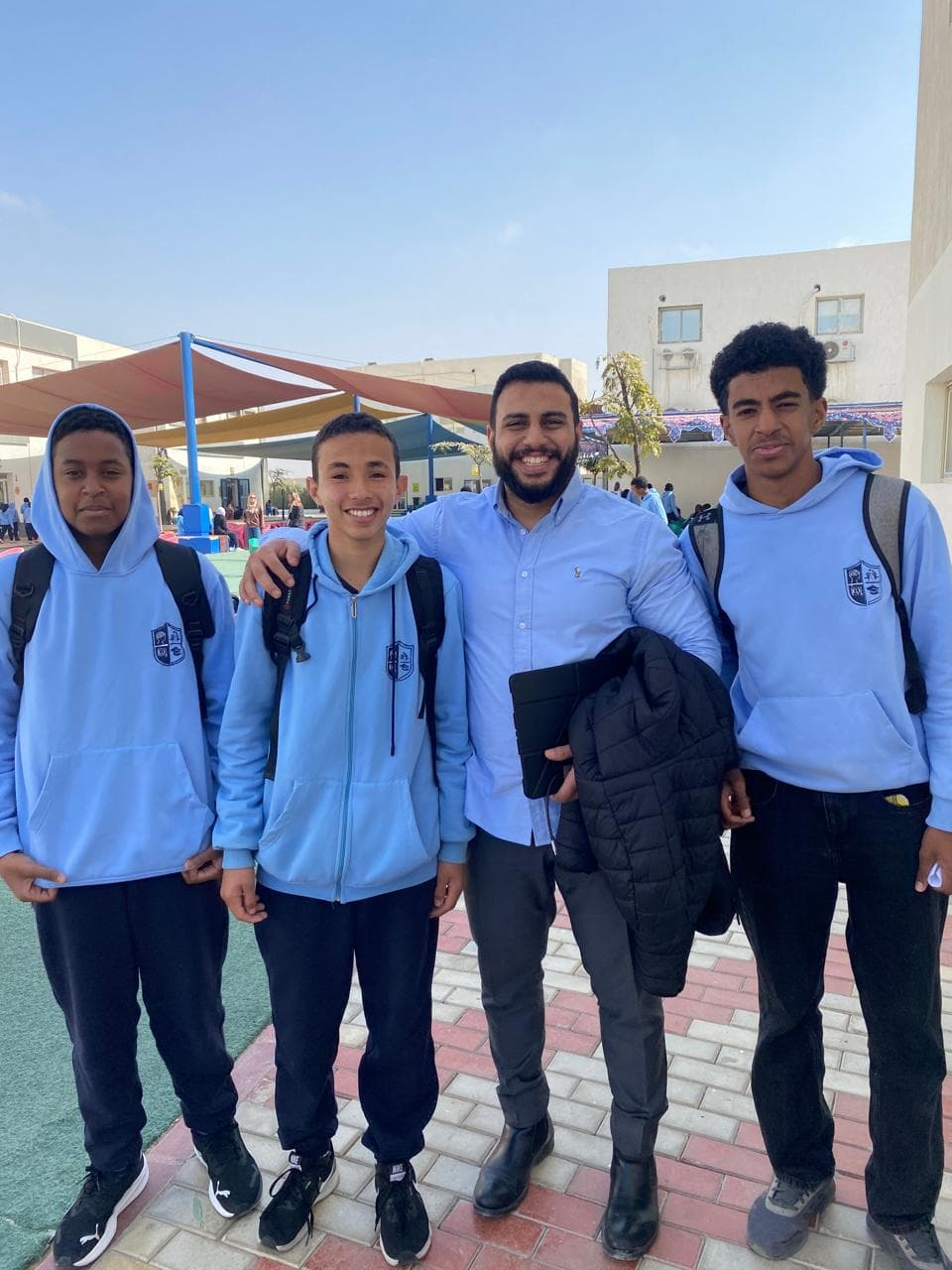 Yousef smiling with three students in school uniform outside after class.